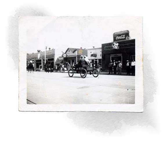 An old black and white photo with shops and vehicles